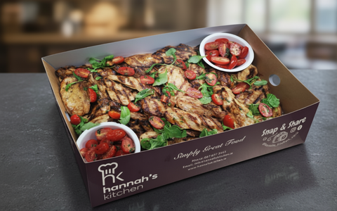 Chargrilled balsamic chicken breast platter with cherry tomatoes and fresh greens in Hannah’s Kitchen catering box