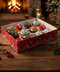 Festive Christmas cupcakes from Hannah’s Kitchen displayed in a rustic holiday scene with a fireplace, holly, and seasonal decorations.