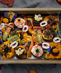 Halloween treat box filled with cupcakes decorated with ghosts, pumpkins, spider webs, and assorted candies in a rustic wooden crate, surrounded by autumn leaves and pumpkins