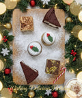 Christmas treat box from Hannah’s Kitchen featuring chocolate biscuit pudding, white chocolate cranberry pudding, and festive desserts on a wooden board with Christmas decorations.