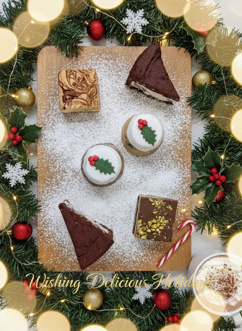 Christmas treat box from Hannah’s Kitchen featuring chocolate biscuit pudding, white chocolate cranberry pudding, and festive desserts on a wooden board with Christmas decorations.