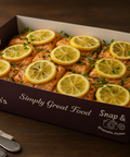 Oven-baked salmon fillets topped with fresh lemon slices and herbs, presented in a Hannah’s Kitchen catering box