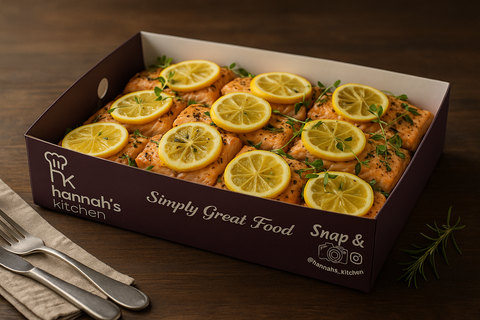 Oven-baked salmon fillets topped with fresh lemon slices and herbs, presented in a Hannah’s Kitchen catering box